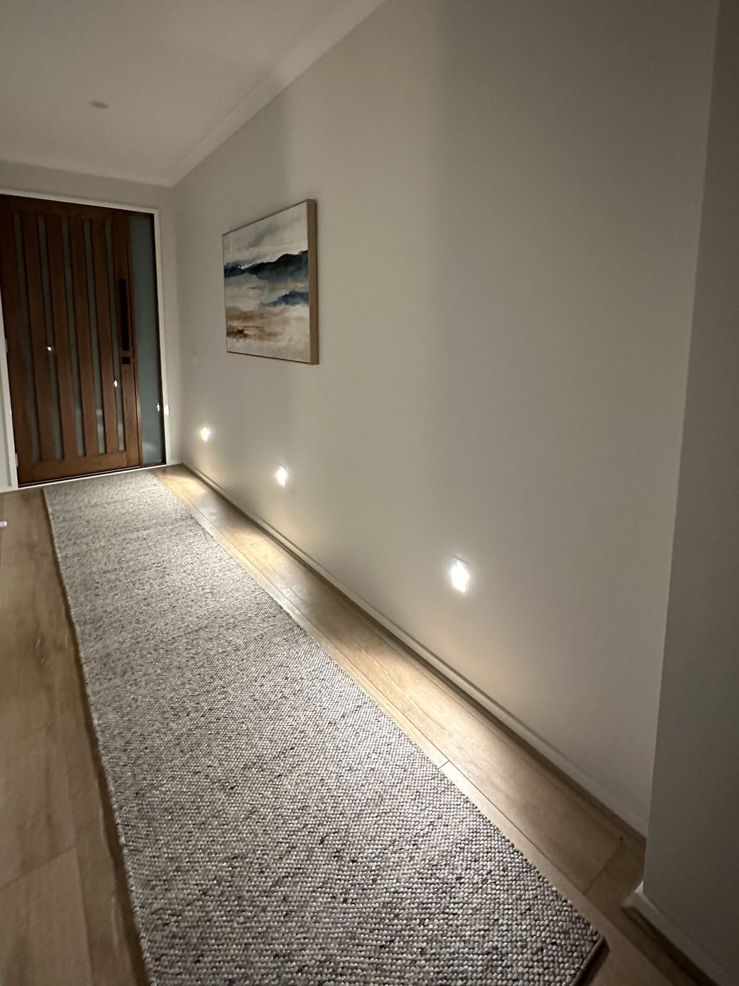 Hallway at night lit by low-level step lights set into the wall along a runner leading to a timber front door, installed by SALTD Electrical