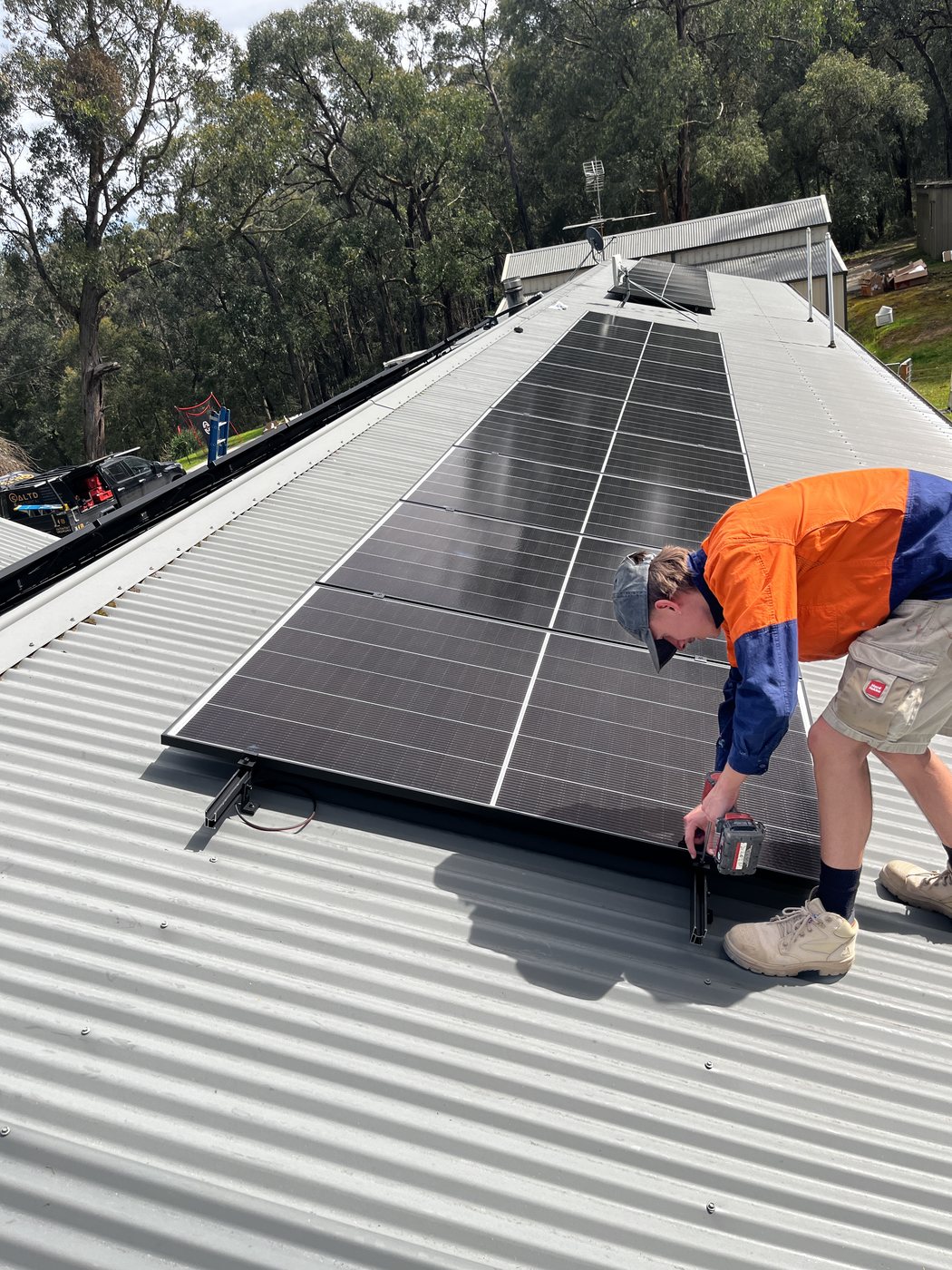 SALTD Electrical tradesman fixing a solar panel to its mounting rail on a steel roof, with the SALTD ute in the driveway below